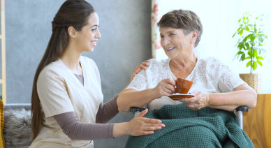 caregiver serving a cup of tea to senior woman while smiling